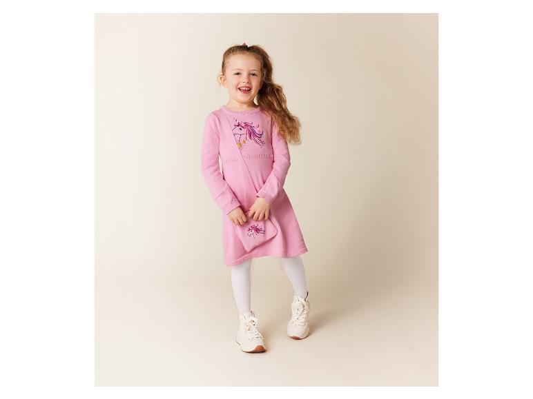 Ein Mädchen trägt ein rosafarbenes Kleid mit Einhorn-Print und einer passenden Tasche.