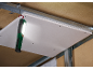 Eine helle Arbeitsleuchte hängt an einem Metalldeckenrahmen und beleuchtet eine Gipskartonplatte.