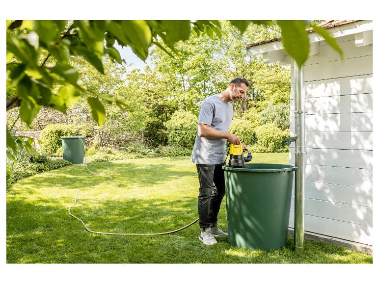 Mann im Garten benutzt eine Pumpe, um Pflanzen aus einem Regenwassertank zu gießen.