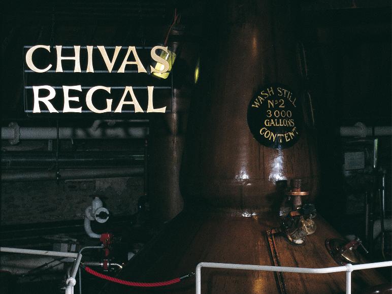 Beleuchtetes Schild einer Whiskymarke über einem großen Kupferkessel in einer Brennerei.