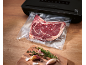 Vakuumiergerät mit einem vakuumierten Steak und Kräutern auf einem Holzbrett.