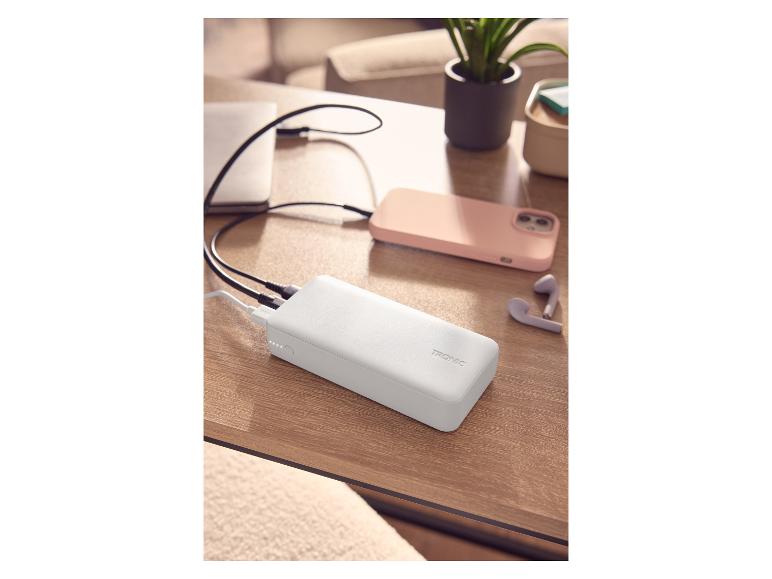 Weiße Powerbank lädt Laptop und Smartphone auf einem Holztisch.