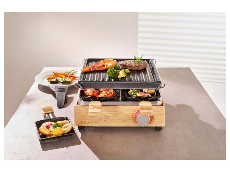 Ein Raclette-Grill aus Bambus mit Fleisch, Garnelen und Gemüse auf dem Grill und in den Pfännchen.