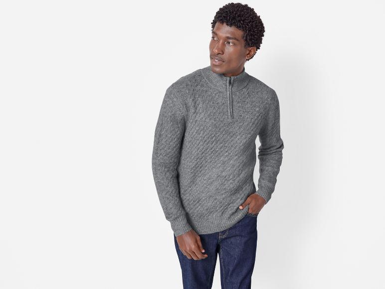 Ein Mann in einem grauen Pullover mit Reißverschluss und Jeans.
