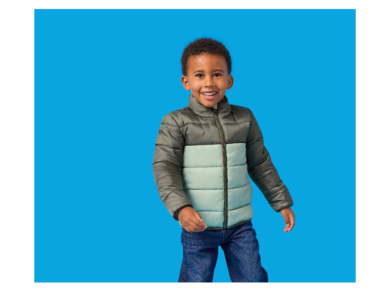 Lächelnder Junge in zweifarbiger Steppjacke und Jeans