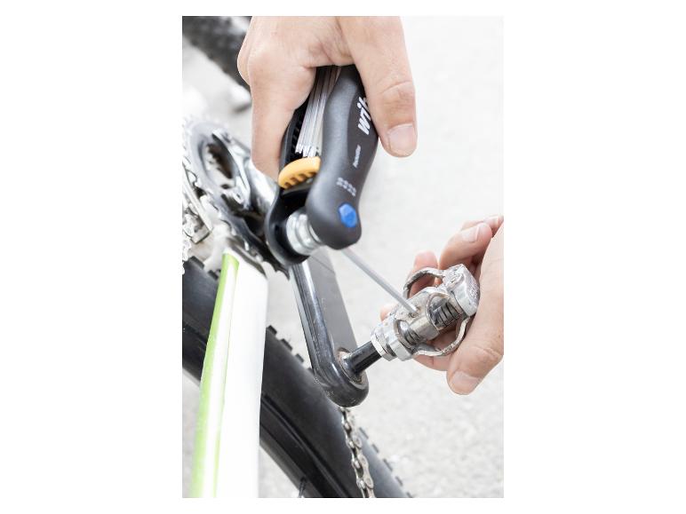 Hände verwenden ein Multitool, um ein Fahrradpedal einzustellen.