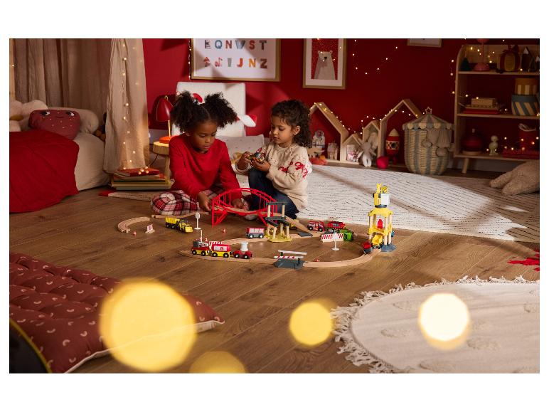 Zwei Kinder spielen mit einer Holzeisenbahn in einem festlichen Zimmer.