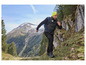 Ein Mann mit Jacke und Hose mit dem Logo 'Exploring the Mountains' geht auf einem Bergpfad.