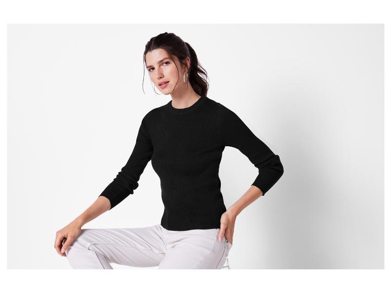 Eine Frau trägt einen schwarzen Pullover und eine weiße Hose.