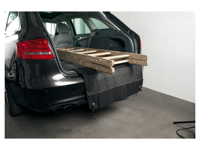 Eine Holzleiter im Kofferraum eines Autos, geschützt durch eine schwarze Stoßfängerabdeckung.