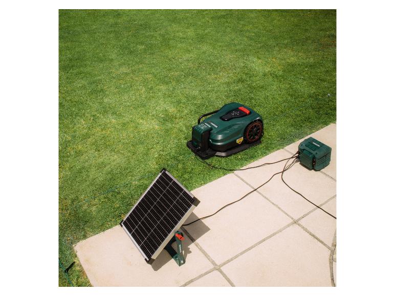 Grüner Mähroboter mit Ladestation und Solarpanel in einem Garten.