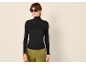 Frau in schwarzem Rollkragenpullover, grüner Hose und Sonnenbrille.