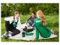Drei Freunde picknicken auf der Wiese mit grünen Kühltaschen und Trinkflaschen.