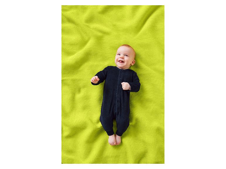 Lächelndes rothaariges Baby in einem schwarzen Strampler, liegend auf einer lindgrünen Decke.