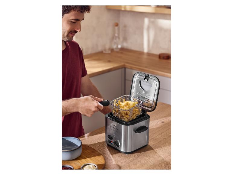 Mann frittiert Pommes in einer Fritteuse auf einer Küchenarbeitsplatte aus Holz