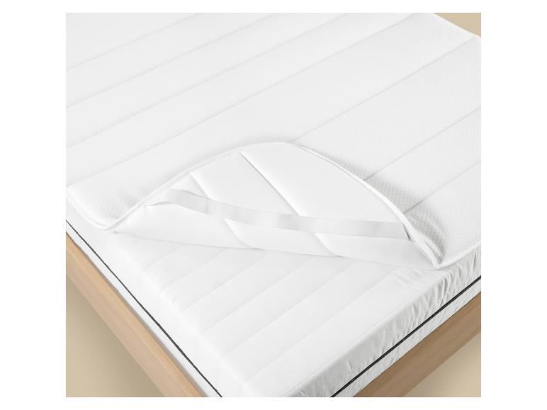 Weißer Matratzenschoner mit Gummibändern auf einem Holzbett.