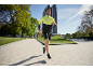 Mann in gelb-schwarzer Laufjacke und schwarzen Shorts joggt im Freien.