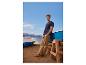 Mann in marineblauem T-Shirt und beiger Hose am Strand, an ein Boot gelehnt.