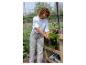 Frau im Gewächshaus hält eine Topfpflanze, mit anderen Pflanzen und Gartenzubehör.