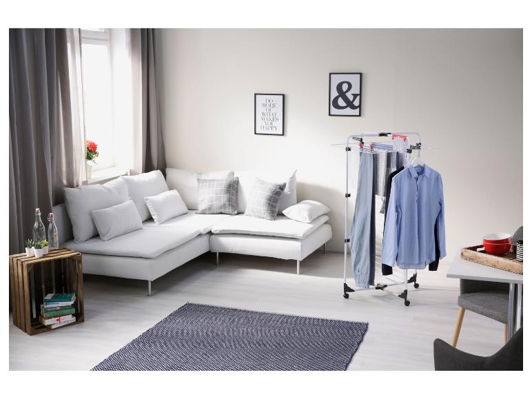 Wäscheständer mit Hemden und Hosen in einem modernen Wohnzimmer mit weißem Sofa und Teppich.