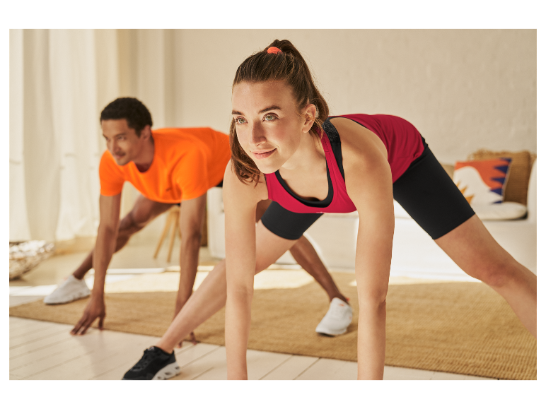 Zwei Personen machen Dehnübungen in ihrer Sportkleidung zu Hause.