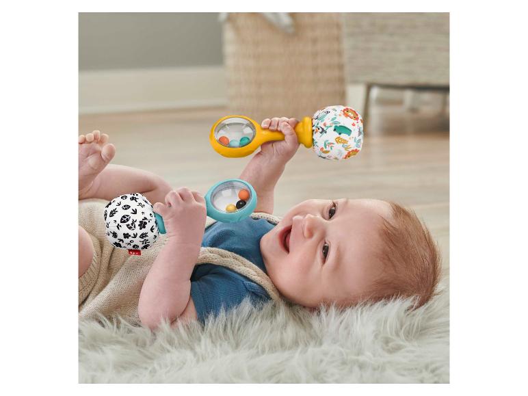 Glückliches Baby spielt mit zwei Fisher-Price Rasseln auf einem flauschigen Teppich.