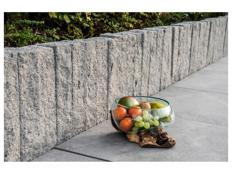 Eine Glasschale mit frischem Obst, darunter Trauben, Mandarinen und Mango, auf einem Holzsockel.