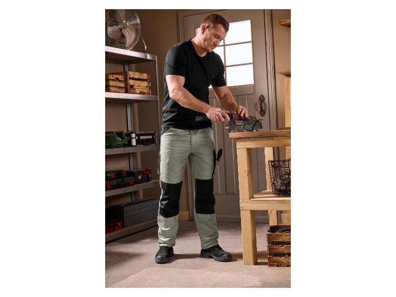Mann in PARKSIDE® Arbeitshose bei der Holzbearbeitung in einer Werkstatt.