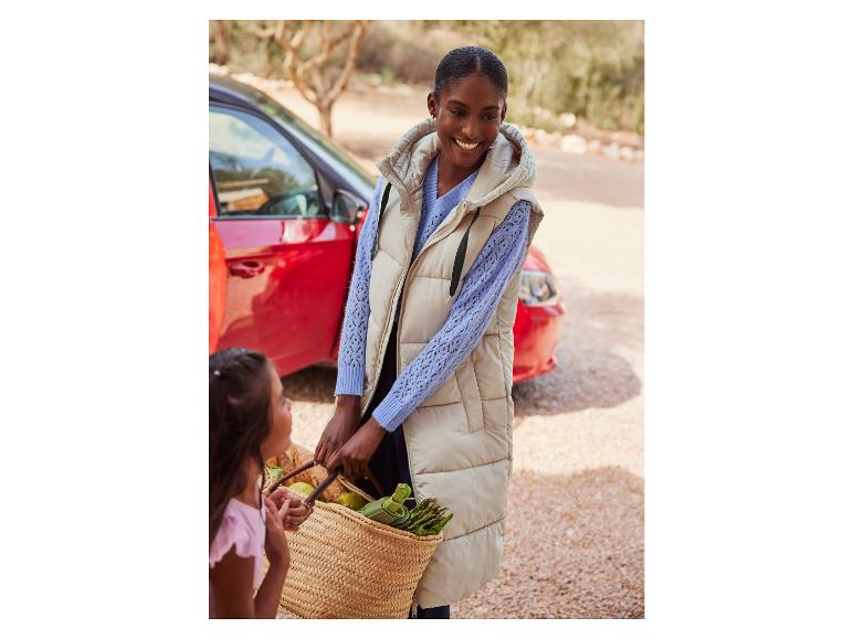 Eine Frau in einer beige Weste trägt einen Einkaufskorb.