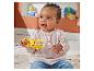 Glückliches Baby spielt mit einer gelben Affenrassel, sitzt auf einem Teppich mit Spielzeug im Hintergrund.