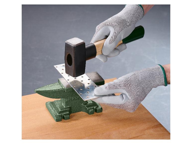 Hände in Handschuhen hämmern eine Metallplatte auf einen Amboss.