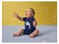 Baby in blauem Haifisch-T-Shirt spielt mit Seifenblasen vor gelbem Hintergrund.