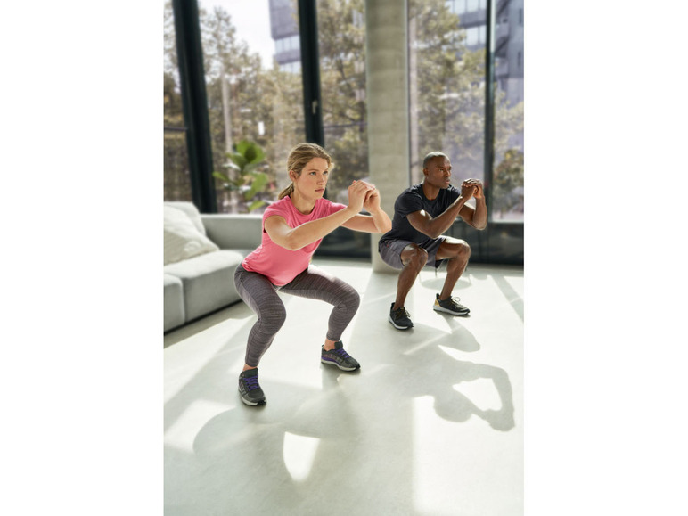 Zwei Personen machen Squats während eines Workouts in einem hellen Raum.