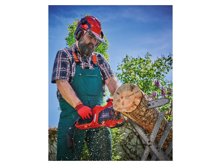 Mann in Schutzkleidung sägt einen Baumstamm mit einer Elektrokettensäge, Sägespäne fliegen.