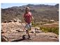 Mann in Wander-T-Shirt und Shorts, mit Trekkingstöcken, in einer Berglandschaft.