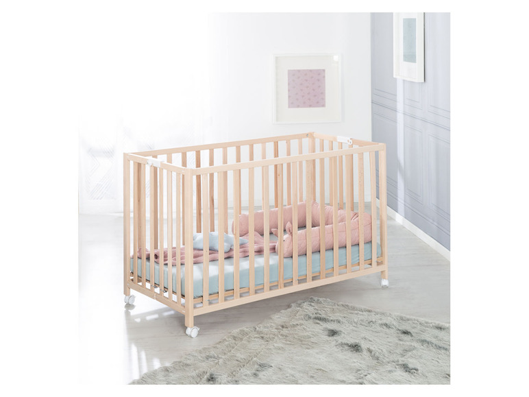 Ein Holzbabybett mit rosa Kissen und einem grauen Teppich.