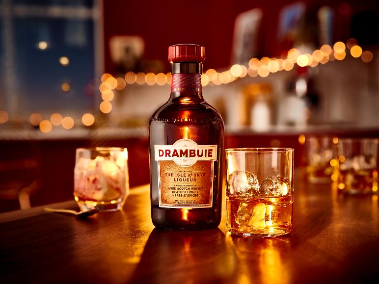 Eine Flasche Drambuie The Isle of Skye Liqueur und ein Glas mit Eis auf einem Holztisch.