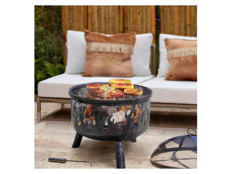 Feuerschale mit Grillrost, Fleisch und Mais, neben Gartenmöbeln.