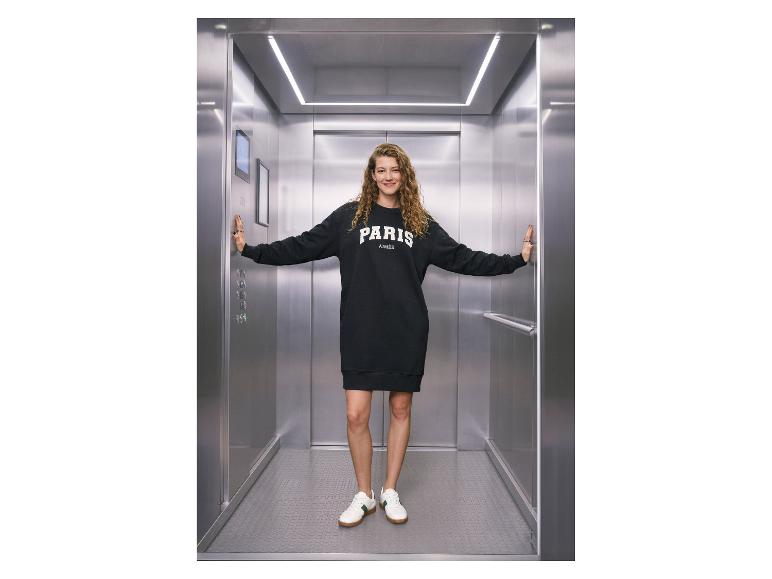 Frau im Aufzug mit ESMARA® Damen Sweatkleid mit der Aufschrift „PARIS AIMÉE“.