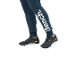 Person trägt dunkelblaue Jogginghose mit weißem Logo und schwarze Sportschuhe.