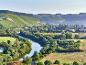 Flusslandschaft mit Weinbergen auf Hügeln und einem Dorf im Hintergrund.