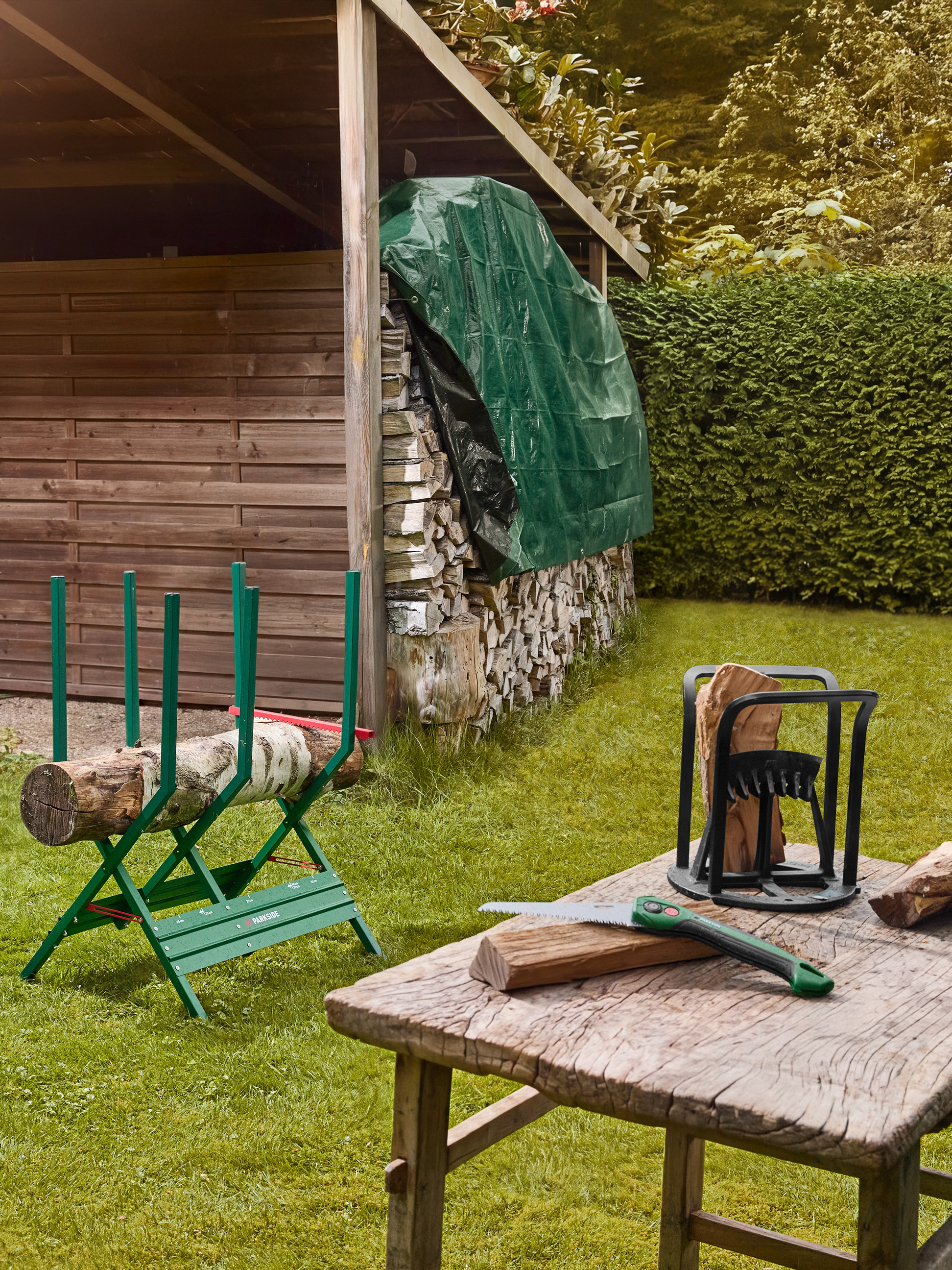 Sägebock und Holzspalter im Freien, mit Säge und Holz auf einem Tisch.