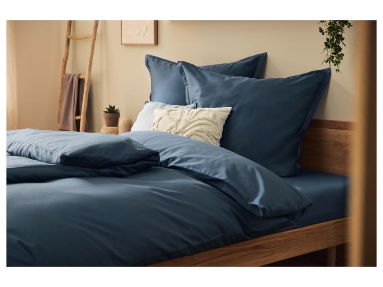 Marineblaue Bettwäsche auf einem Holzbett mit Dekokissen und Pflanzen.