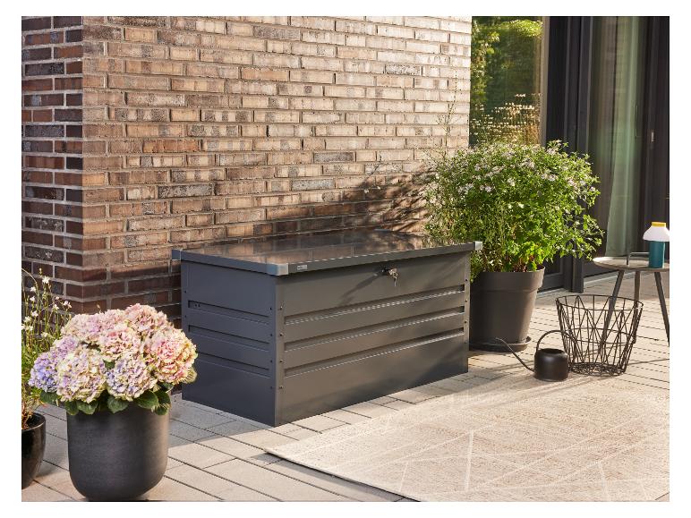 Dunkelgraue Gartenbox mit Schlüssel, Topfpflanzen und Teppich auf einer Terrasse.