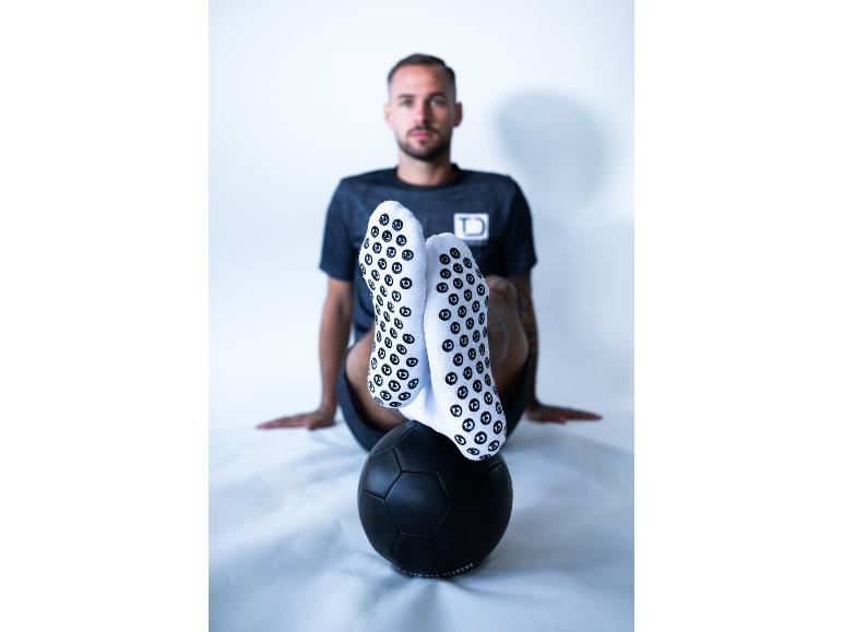 Mann in schwarzem T-Shirt und weißen Socken mit Anti-Rutsch-Noppen, die Füße auf einem schwarzen Ball.
