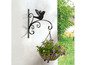Ein schwarzer, verzierter Blumentopfhalter mit Vogelmotiv, an einer Wand befestigt.