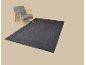 Grauer Sessel mit Holzrahmen und dunkler Teppich mit geometrischem Muster.