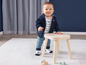 Ein Baby in einem blauen Pullover und Hose steht auf einem Holzhocker.