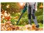 Person benutzt einen Laubbläser, um Herbstlaub im Garten zu entfernen.