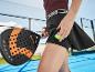Frau auf einem Padel-Platz mit Schläger und Ball in der Tasche, in Sporttop und Rock.